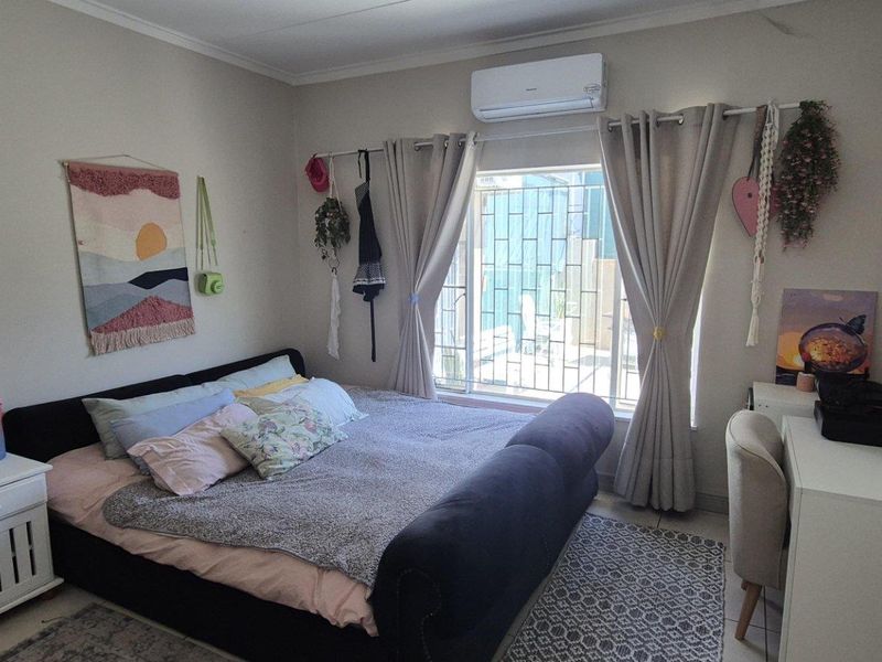 A functional bedroom featuring tiled flooring, a wall-mounted split-system air conditioner, and a window fitted with security bars.