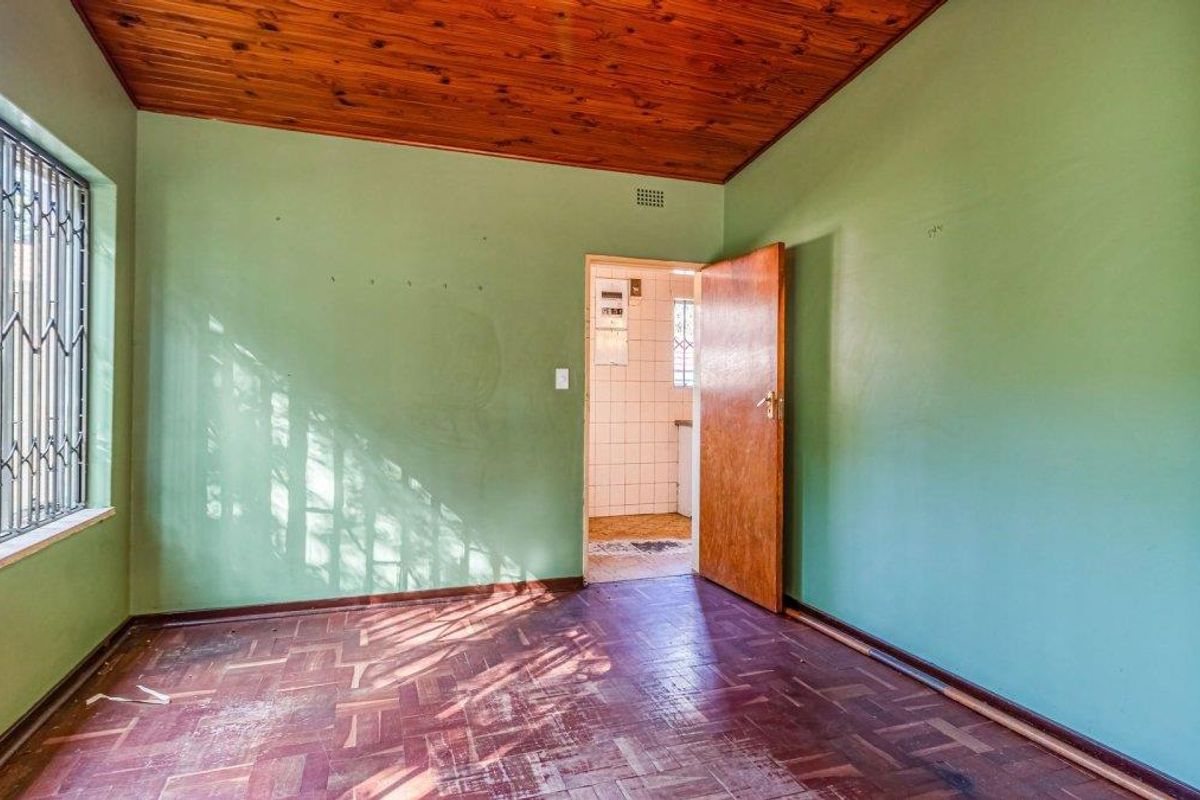 An empty bedroom featuring parquet flooring, a timber ceiling, and a security gate on the window, leading to an adjacent tiled area.