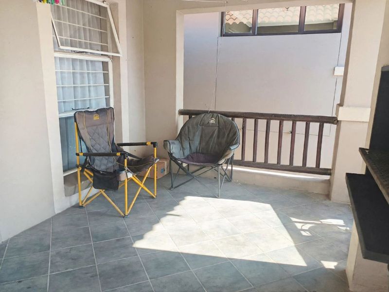 A covered patio area featuring tiled flooring, a wooden balustrade, and a built-in braai, offering a functional outdoor space for relaxation.