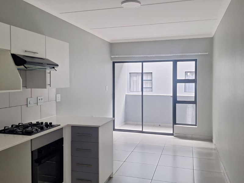 Modern open-plan kitchen and living area featuring tiled floors, built-in cabinetry, gas hob, and sliding door access to a private balcony.