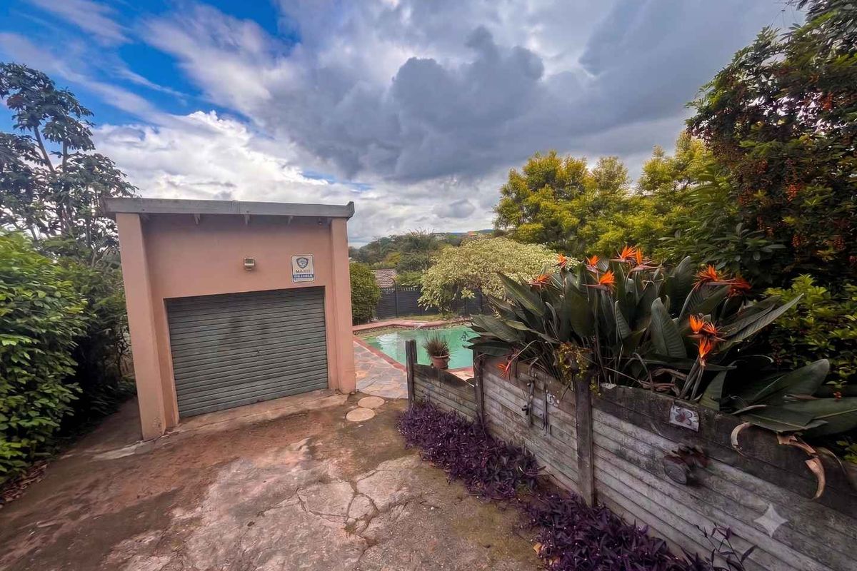 Rear exterior view featuring a detached garage, concrete driveway with visible cracking, and a swimming pool area surrounded by established garden landscaping.