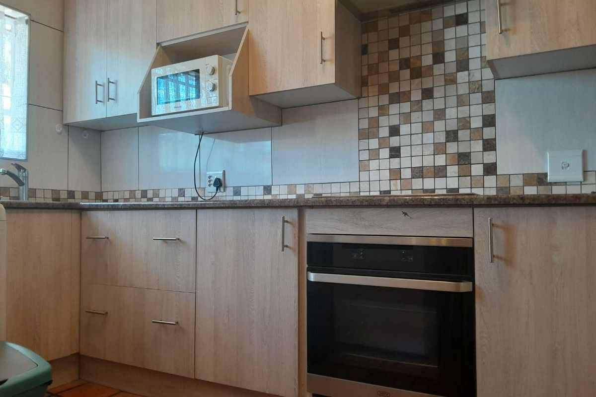 A functional kitchen featuring light wood-grain cabinetry, a built-in oven, extractor fan, and a mosaic tile backsplash with stone-look countertops.