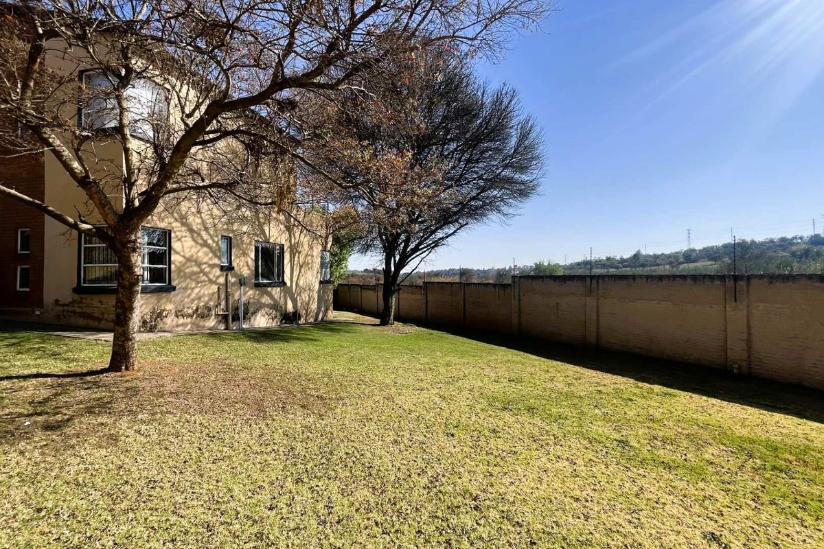 Rear view of the townhouse featuring a private lawn, mature trees, and a perimeter wall with security fencing.