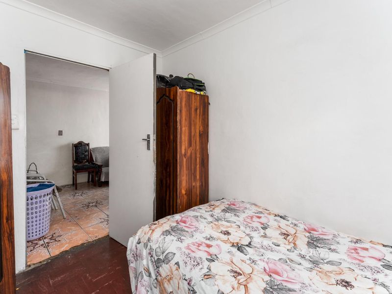 A compact bedroom featuring timber flooring and white walls, with an open doorway leading to an adjacent tiled living area.