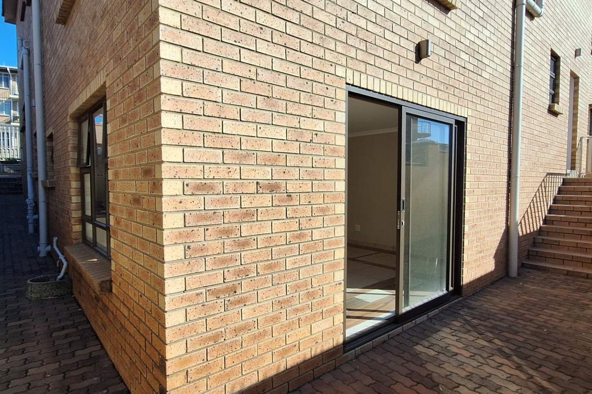 Rear exterior view of the property featuring a paved courtyard, face brick facade, and a sliding glass door providing access to the interior.
