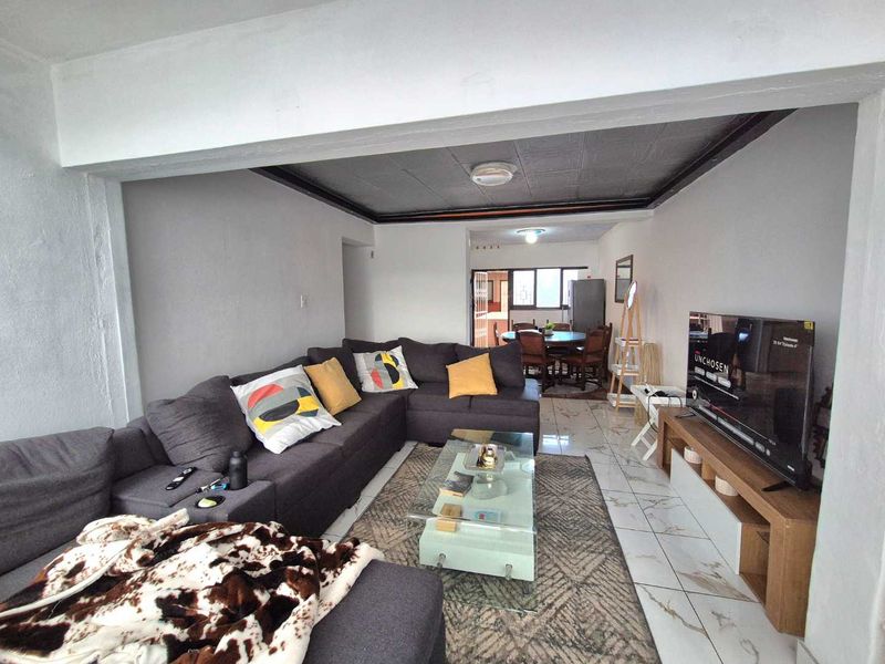 An open-plan living and dining area featuring tiled flooring and a recessed ceiling design, creating a connected space for relaxation and meals.