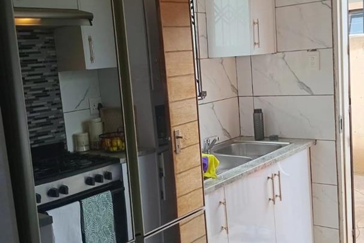 Modern kitchen featuring white cabinetry, marble-look wall tiles, a built-in gas stove with extractor fan, and a double stainless steel sink.