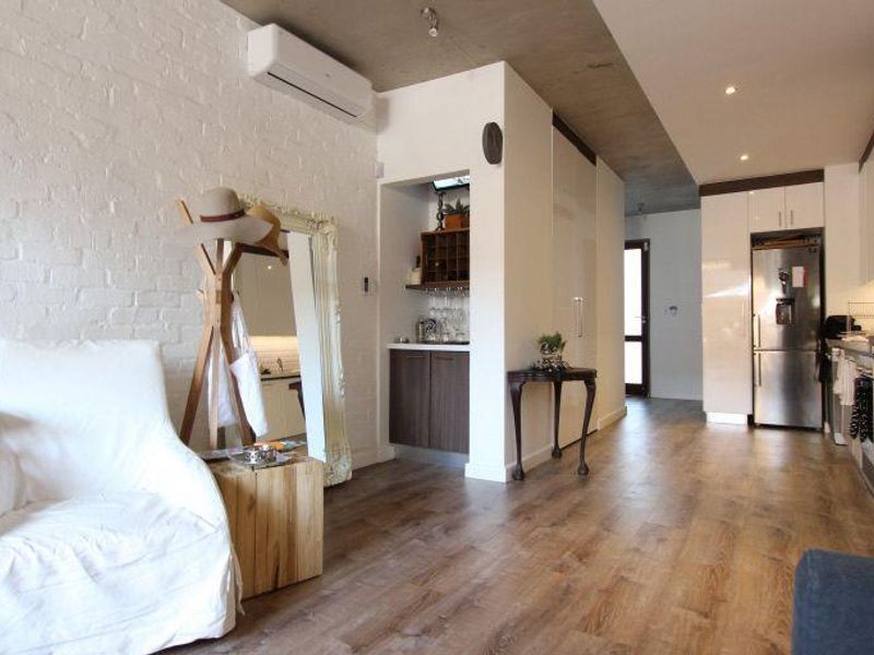 Modern open-plan living area featuring exposed concrete ceilings, brick feature wall, split-system air conditioning, and sleek built-in kitchen cabinetry with integrated appliances.