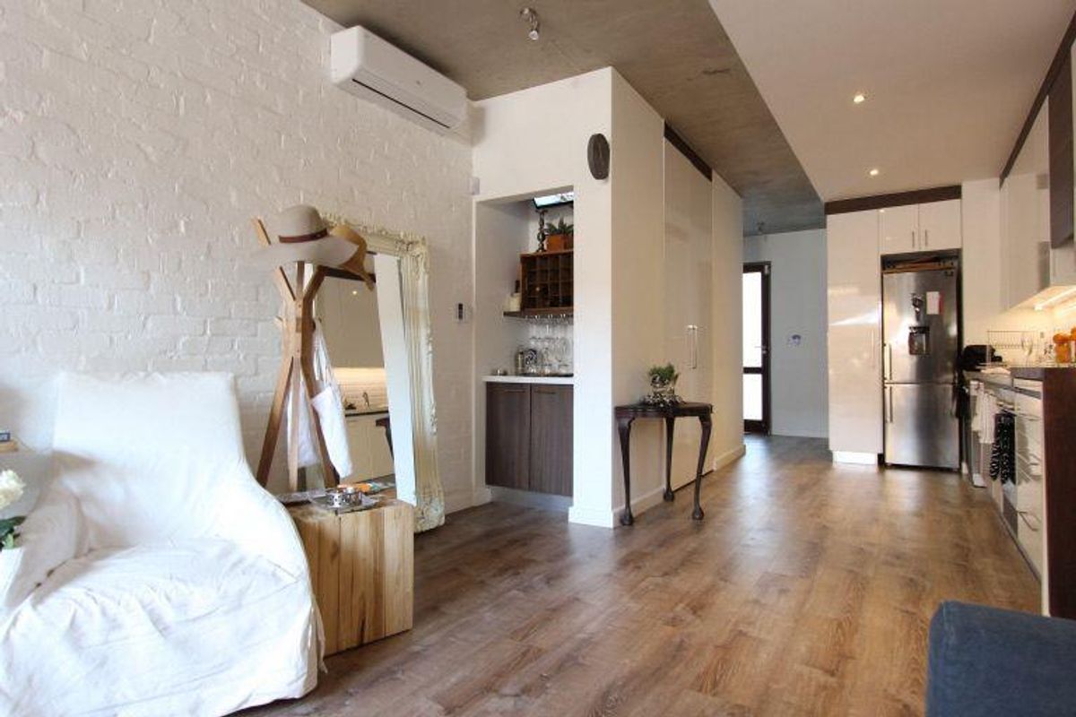 Modern open-plan living area featuring exposed concrete ceilings, brick feature wall, split-system air conditioning, and sleek built-in kitchen cabinetry with integrated appliances.