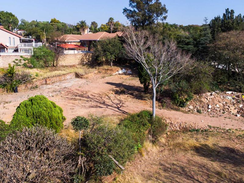 Aerial view of a vacant residential plot featuring mature trees, a retaining wall, and cleared land ready for development.