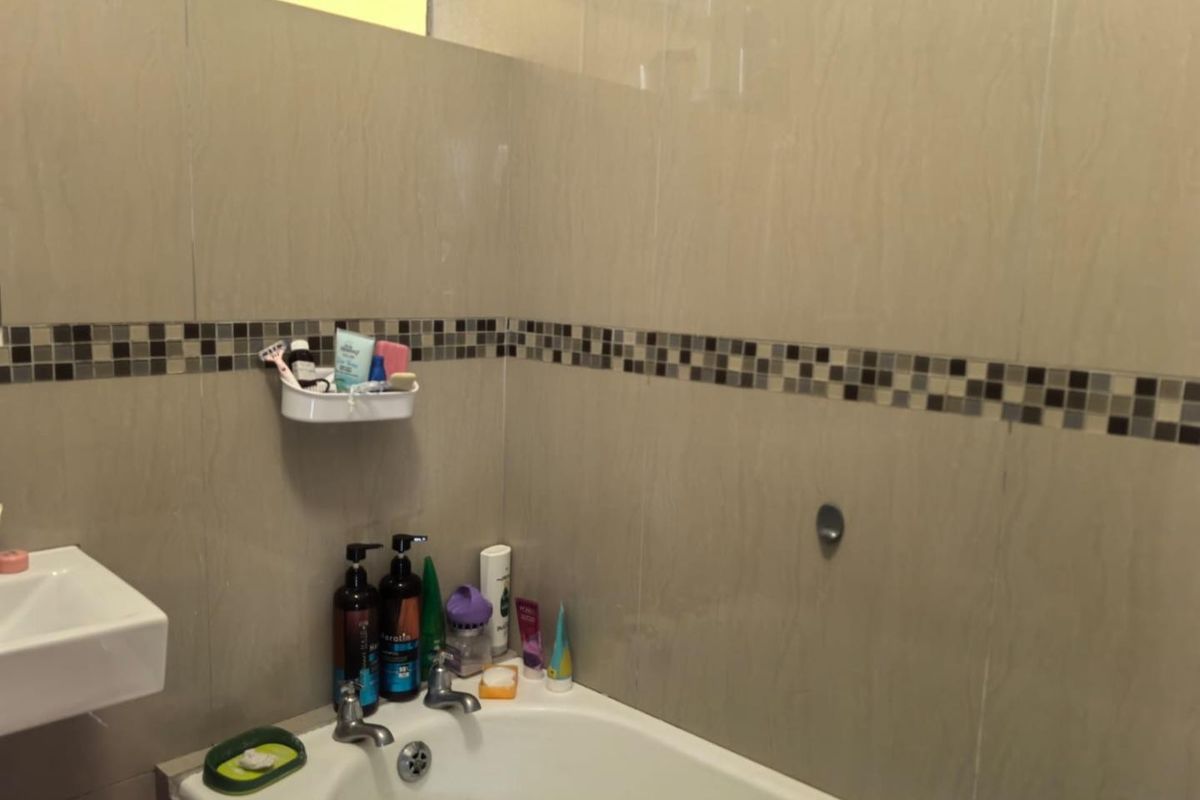 A functional bathroom featuring a built-in bathtub, wall-mounted basin, and neutral wall tiling with a decorative mosaic border.