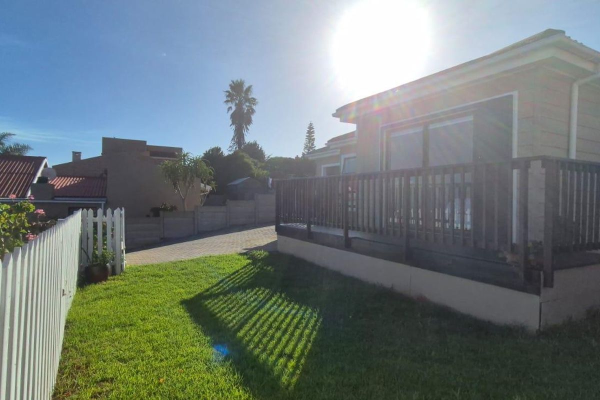 Rear view of the townhouse featuring a timber deck with balustrade, a white picket fence, and a paved driveway area.