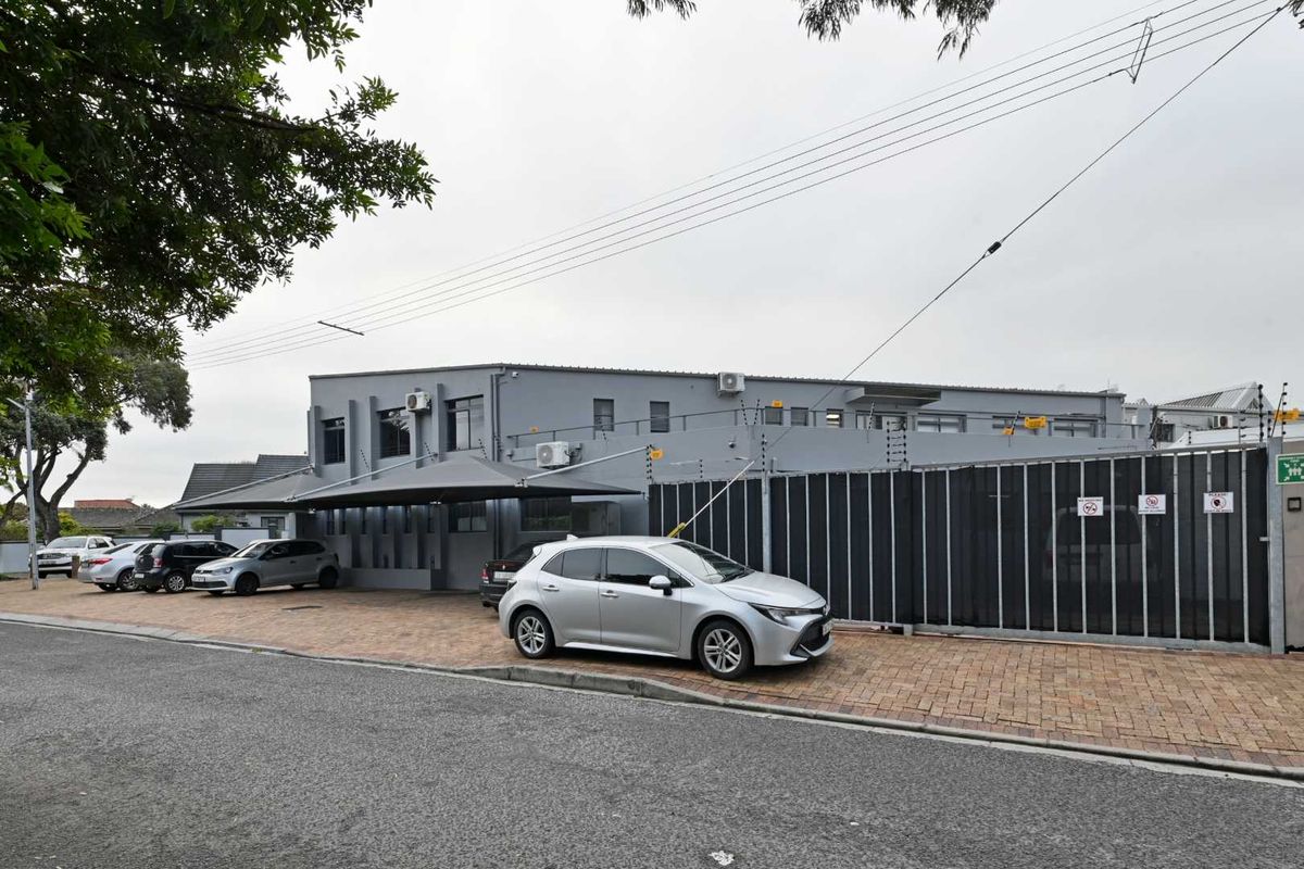 Front exterior view of a commercial property featuring a paved driveway, secure perimeter fencing, and dedicated shade port parking.