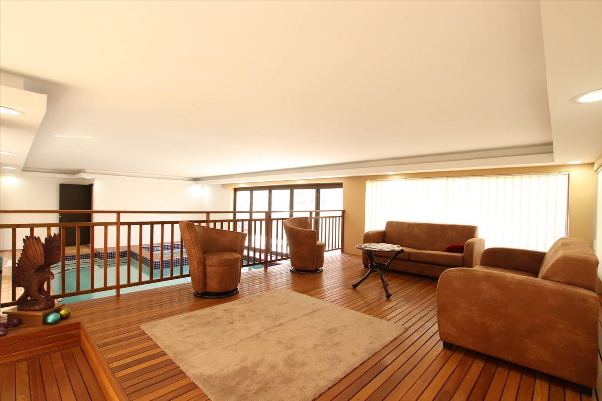An indoor living area featuring timber flooring and a mezzanine-style balcony overlooking an integrated indoor swimming pool.