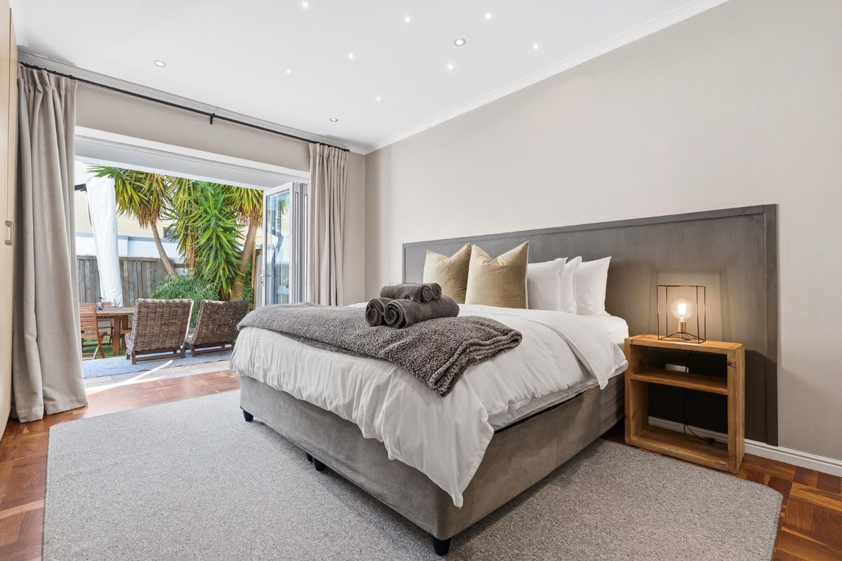 Spacious bedroom featuring elegant parquet flooring, recessed downlighting, and large bi-fold doors providing seamless access to a private outdoor patio area.