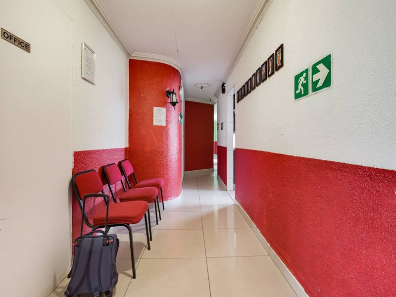 A commercial-style hallway featuring tiled flooring, coved ceilings, and red and white painted walls with emergency exit signage.