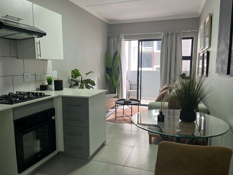 Modern open-plan apartment featuring a compact kitchen with built-in appliances, tiled flooring, and a sliding door leading to a private balcony.