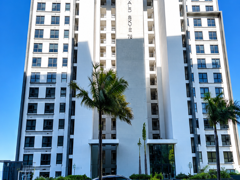 Front elevation of the Emerald Skye apartment building, featuring a modern white facade, paved driveway, and landscaped exterior planters.
