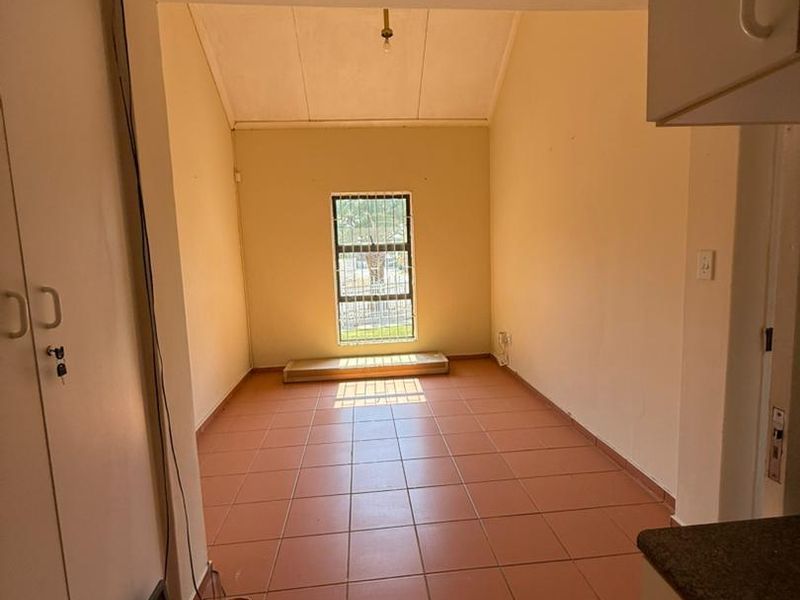An empty living area featuring tiled flooring, built-in storage cupboards, and a vaulted ceiling with a window fitted with security bars.