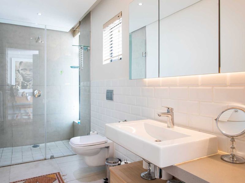 Modern bathroom featuring a walk-in glass shower, wall-mounted toilet, vanity basin with mixer tap, and a sleek mirrored medicine cabinet with integrated lighting.