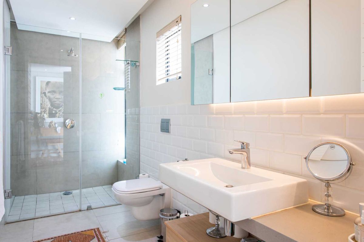 Modern bathroom featuring a walk-in glass shower, wall-mounted toilet, vanity basin with mixer tap, and a sleek mirrored medicine cabinet with integrated lighting.