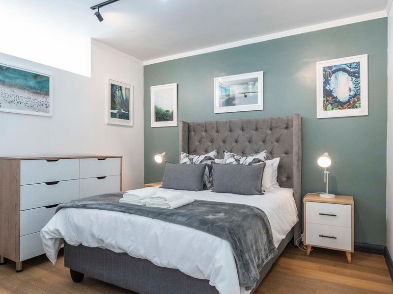 A well-maintained bedroom featuring modern track lighting, laminate flooring, and a feature wall, providing a clean and comfortable living space.