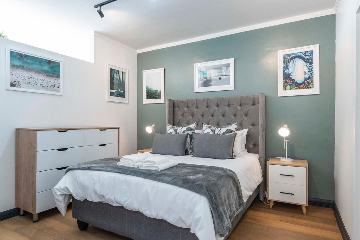 A well-maintained bedroom featuring modern track lighting, laminate flooring, and a feature wall, providing a clean and comfortable living space.
