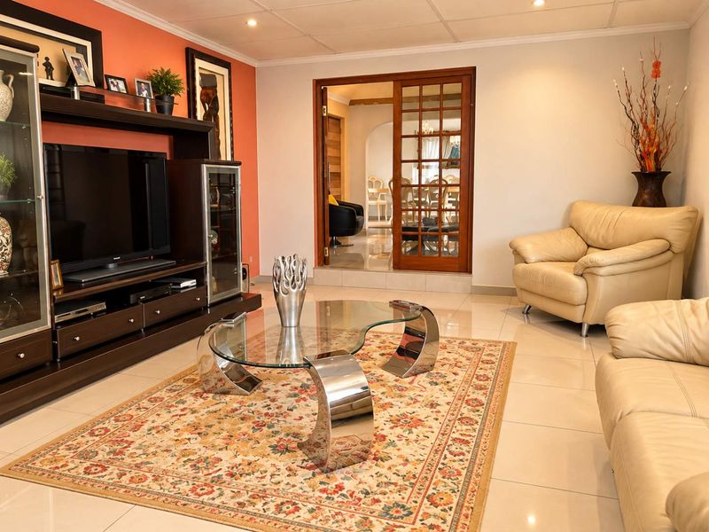 A well-maintained living room featuring polished tiled flooring, recessed ceiling lights, and elegant wooden-framed glass sliding doors leading to an adjacent space.