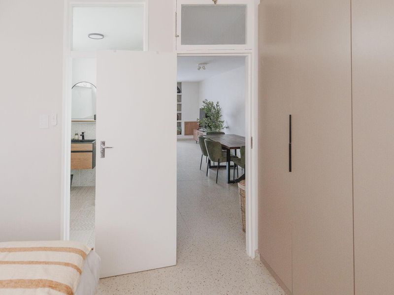 A bright bedroom featuring modern terrazzo flooring, a large built-in wardrobe, and a view through to the adjacent bathroom and living area.