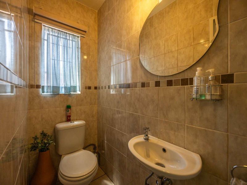 A compact guest bathroom featuring neutral ceramic wall tiles, a wall-mounted basin, and a standard toilet.