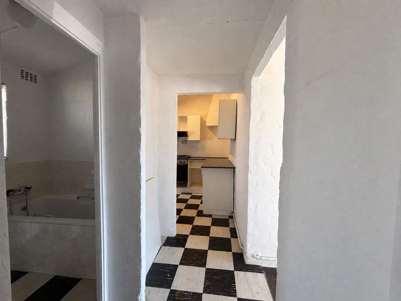 A hallway view connecting to a bathroom and a kitchen area, featuring checkerboard flooring and basic built-in cabinetry.
