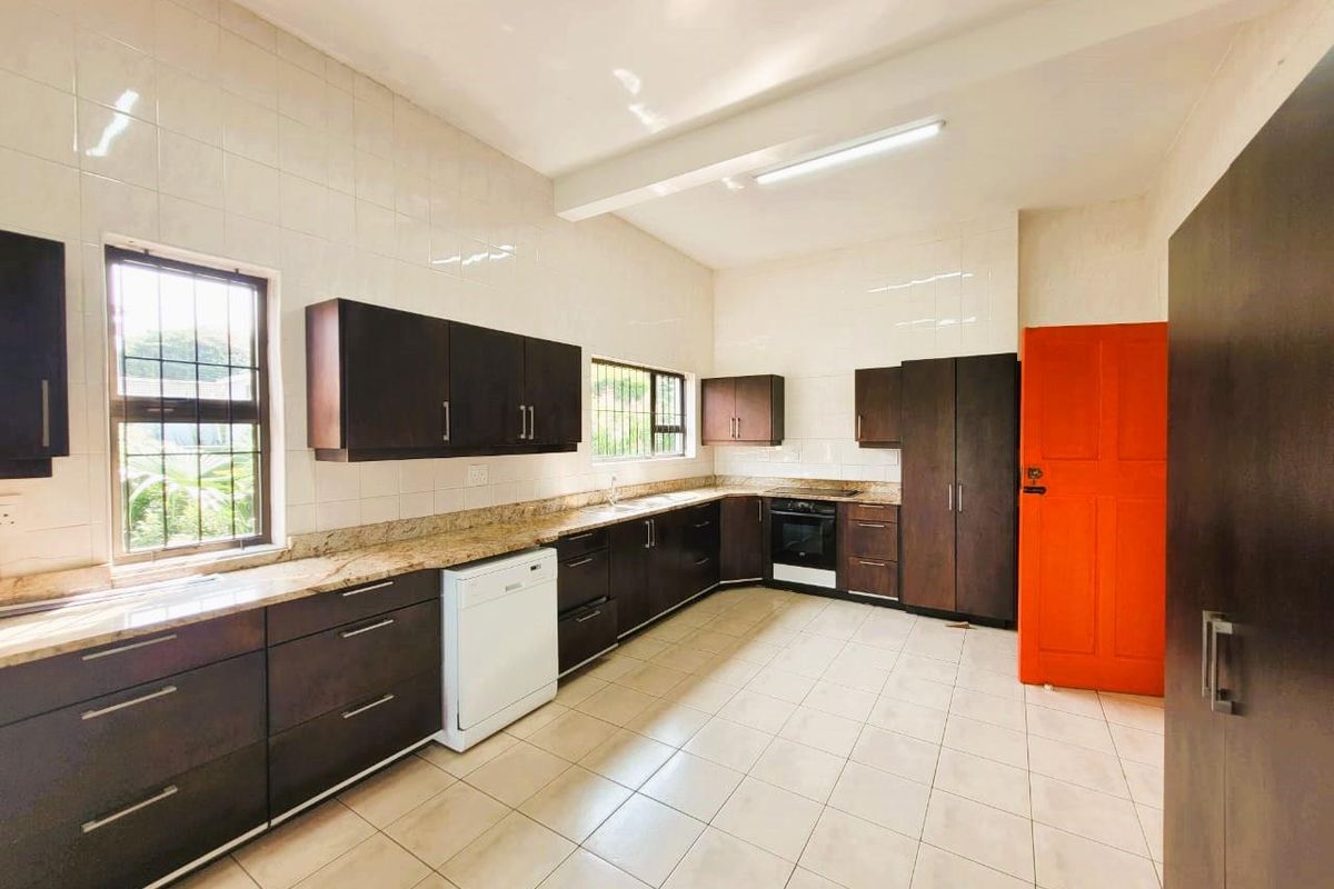 A functional kitchen featuring dark wood cabinetry, granite countertops, tiled walls, and a built-in oven with an extractor fan.
