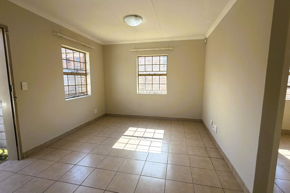 A vacant bedroom featuring neutral wall paint, tiled flooring, and multiple windows providing natural light.
