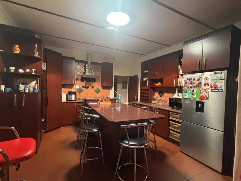 A functional kitchen featuring dark wood cabinetry, a central island with seating, tiled backsplash, and tiled flooring.