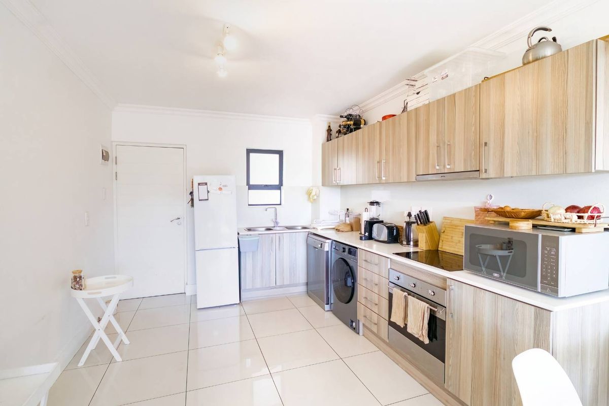A functional kitchen featuring light wood-grain cabinetry, tiled flooring, a built-in oven, hob, and extractor fan, with space for integrated appliances.