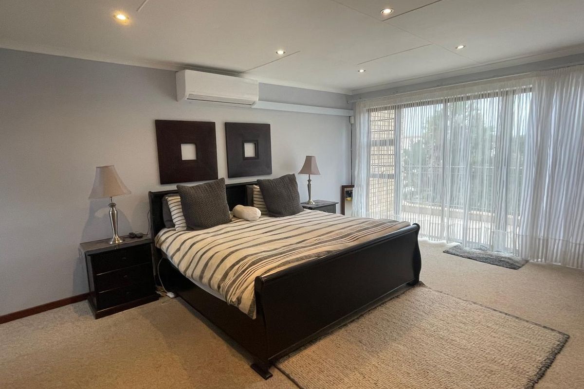 Spacious bedroom featuring neutral carpeting, recessed ceiling lighting, and a wall-mounted air conditioning unit, with direct access to an outdoor balcony.