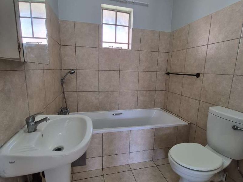 A functional bathroom featuring a pedestal washbasin, built-in bathtub with handheld shower, and standard toilet, finished with neutral ceramic wall and floor tiling.