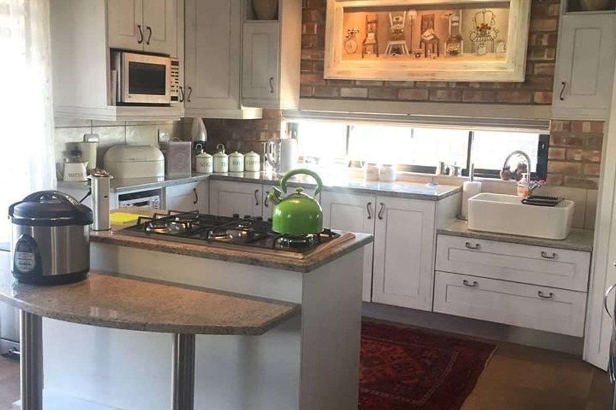 A well-appointed kitchen featuring white cabinetry, granite countertops, a farmhouse-style sink, a gas hob, and a decorative exposed brick backsplash.