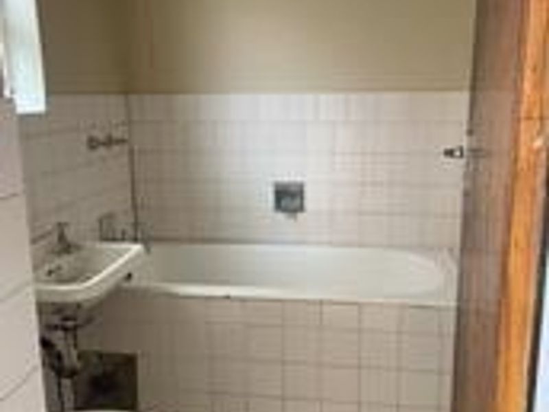 A dated bathroom featuring a standard bathtub, pedestal sink, toilet, and tiled finishes, requiring modernization to improve its overall condition and appeal.