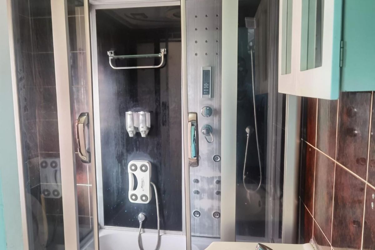 A bathroom featuring a built-in massage shower cabin with integrated controls and tiled wall finishes.