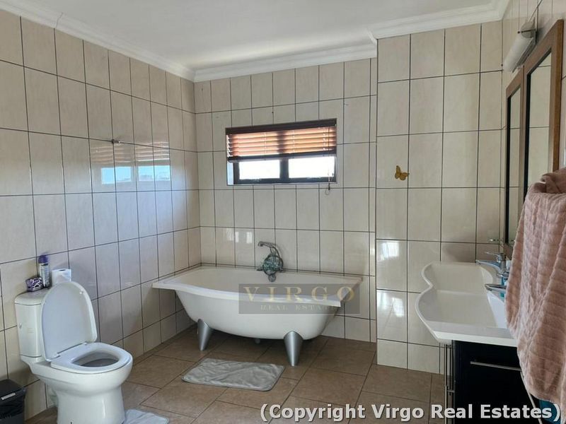 A functional bathroom featuring a freestanding bathtub, wall-mounted basin, and toilet, finished with neutral wall and floor tiles.