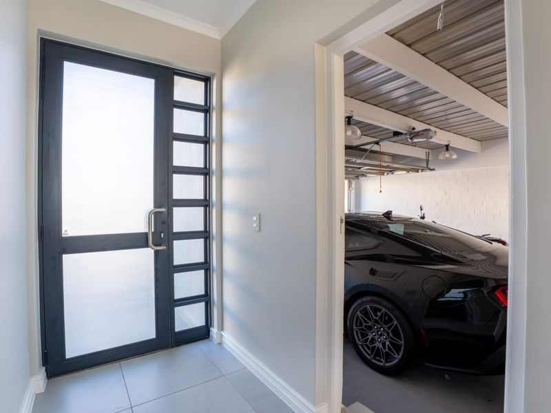 A bright entrance hall featuring a modern frosted glass front door, neutral tiled flooring, and direct internal access to the garage.