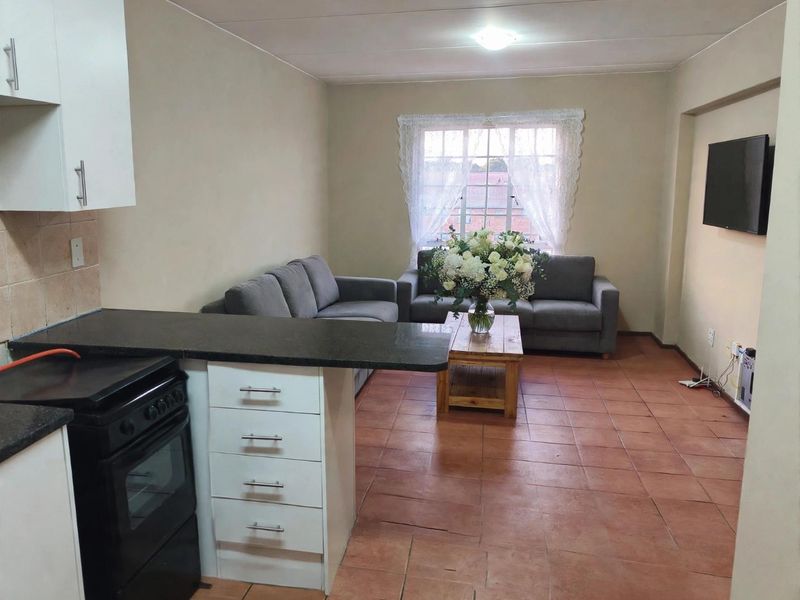 Open-plan living area featuring a functional kitchen with granite countertops and tiled flooring, seamlessly flowing into a comfortable lounge space.