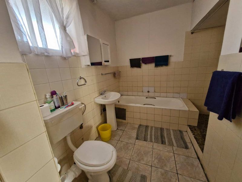 A functional bathroom featuring a pedestal basin, built-in bathtub, and tiled finishes, offering potential for modernization and cosmetic updates.