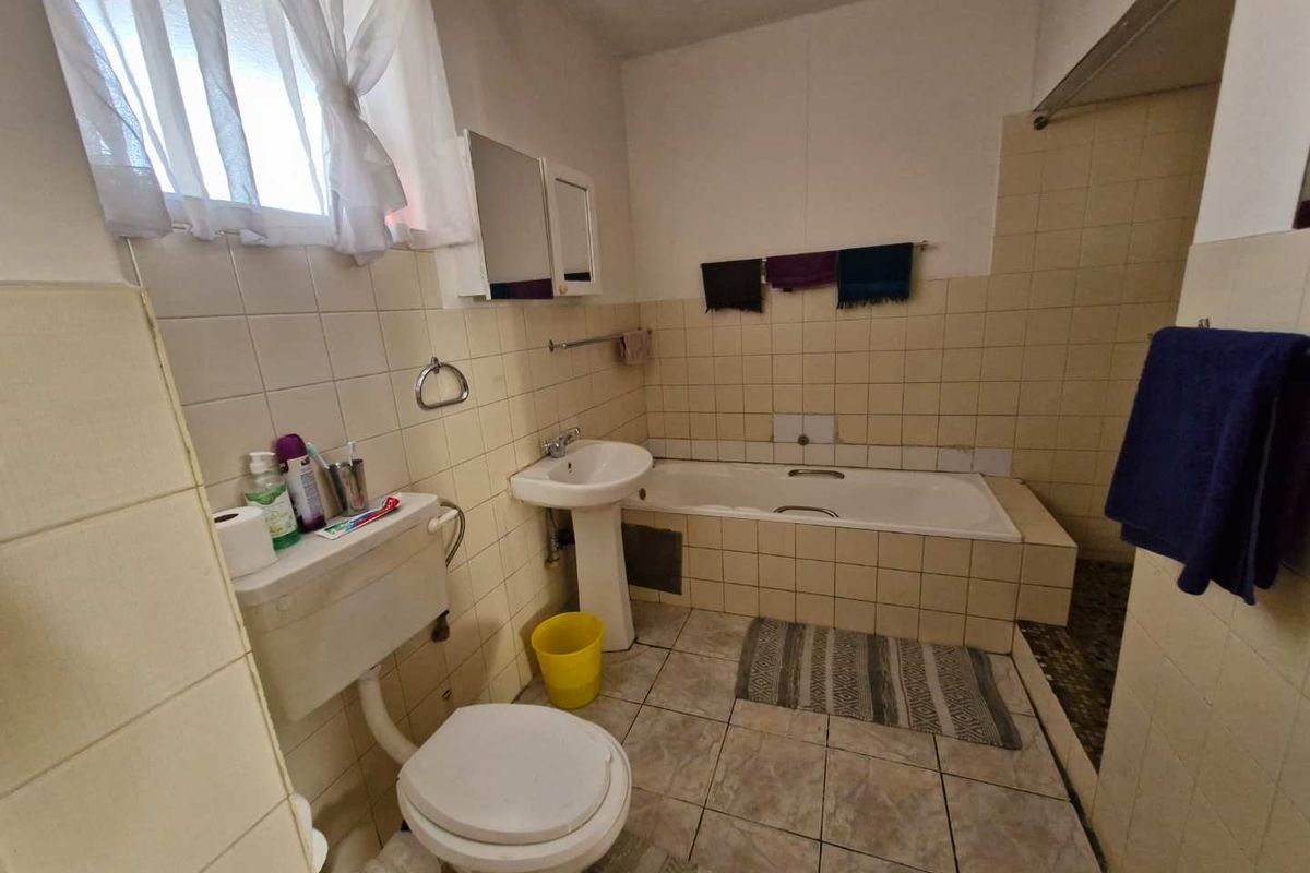 A functional bathroom featuring a pedestal basin, built-in bathtub, and tiled finishes, offering potential for modernization and cosmetic updates.