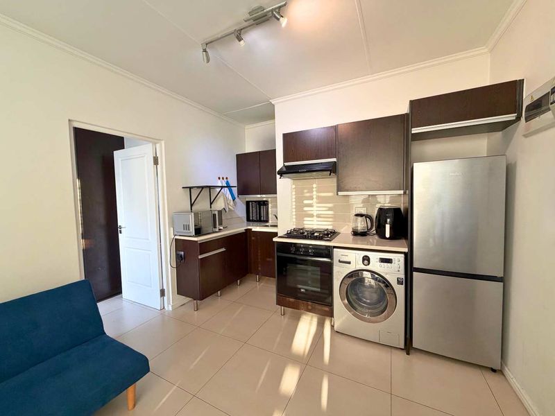 Open-plan kitchen area featuring dark wood cabinetry, built-in oven and hob, extractor fan, and tiled flooring, seamlessly integrated into the living space.