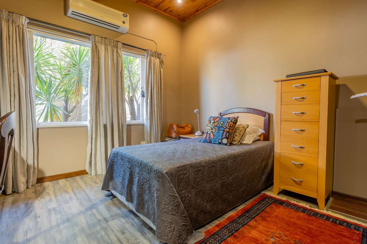 A cozy bedroom featuring timber ceiling detailing, laminate flooring, and a wall-mounted split-system air conditioning unit.