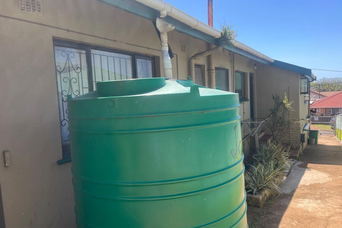 Rear exterior view of the property featuring a large water storage tank, guttering system, and security bars on the windows.