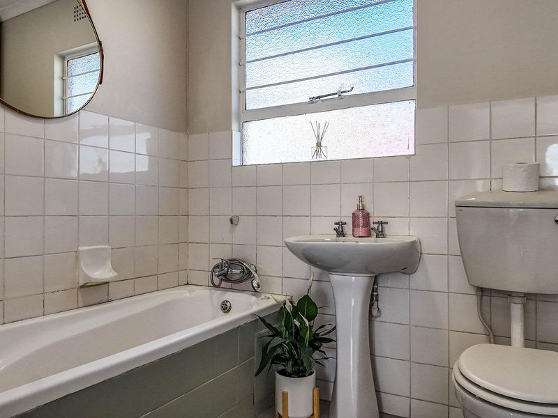 A functional bathroom featuring a standard bathtub, pedestal basin, and toilet, finished with classic white wall tiles and a louvered window for ventilation.