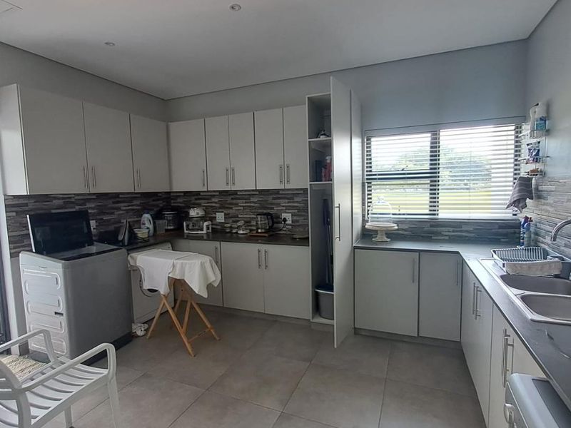 A functional scullery featuring ample built-in cabinetry, a double basin sink, tiled splashbacks, and neutral floor tiles, providing efficient workspace and storage.